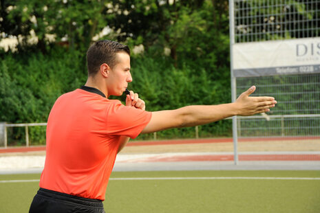 Schiedsrichter mit orangefarbenem T-Shirt und Schiedsrichterpfeide