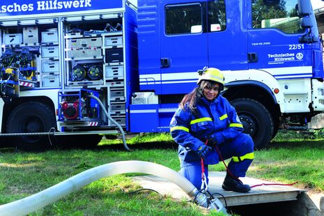 Eine junge Frau in blauem Overall und Helm, im Hintergrund ein blauer Lkw des THW